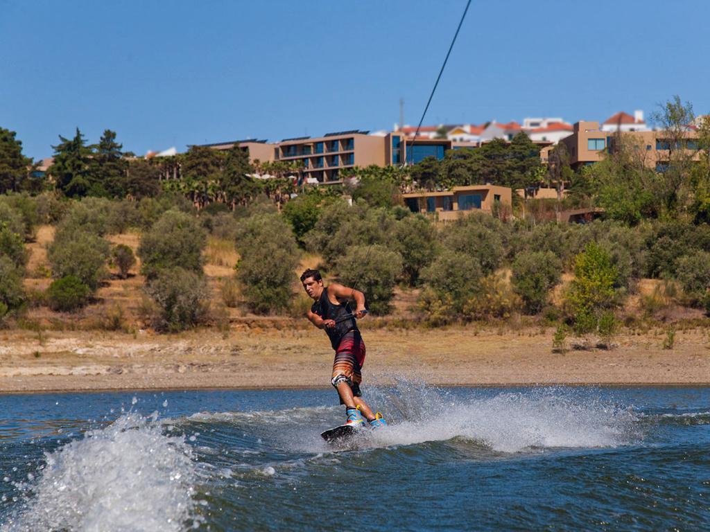 Ap Lago Montargil - Conference & Spa Exterior photo The photo shows a person wakeboarding on a body of water. The individual is being pulled by a cable, which is likely connected to a boat or a winch. The person is wearing a life jacket and swim shorts, balancing on the board as they enjoy the activit