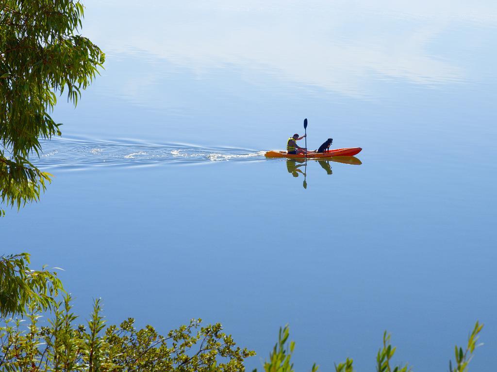 Ap Lago Montargil - Conference & Spa Exterior photo The photo shows a serene scene of a person kayaking on a calm body of water. The surface of the water is very smooth, reflecting the surroundings, and there is a gentle wake behind the kayak indicating movement. The kayaker is wearing a life jacket a