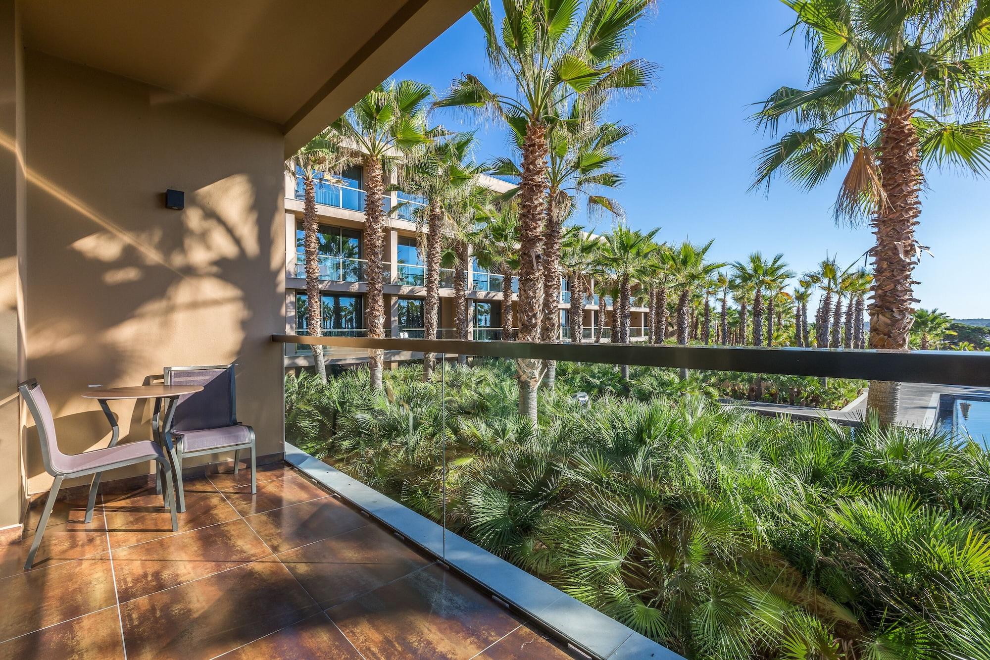 Ap Lago Montargil - Conference & Spa Exterior photo The photo shows a balcony with modern furniture, including a chair and a small table. In the background, there are tall palm trees and lush greenery, suggesting a tropical or resort-like setting. The buildings in the distance are likely part of a hot