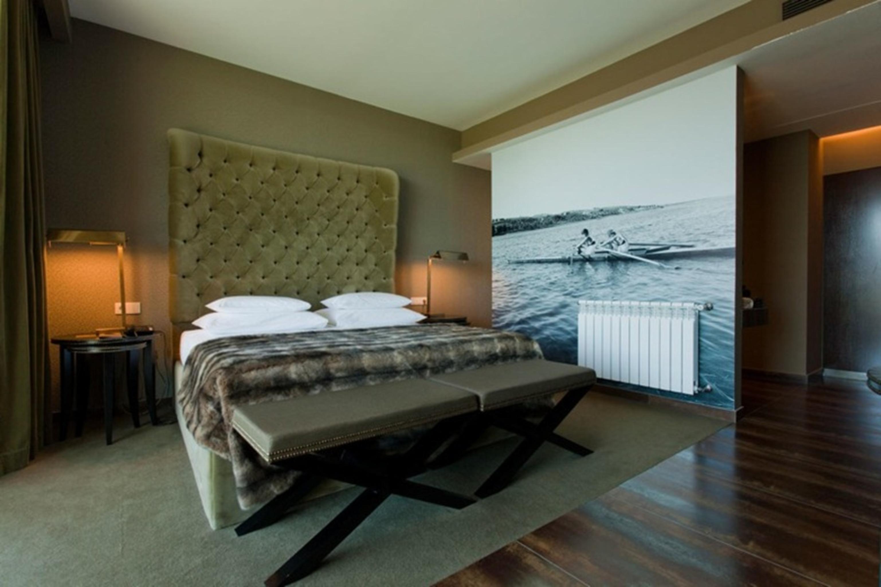 Ap Lago Montargil - Conference & Spa Exterior photo The photo shows a modern hotel room featuring a large bed with a tufted headboard and plush bedding. The color palette is neutral, with shades of green and gray. On one side of the room, there are bedside tables with lamps. A comfortable bench sits a