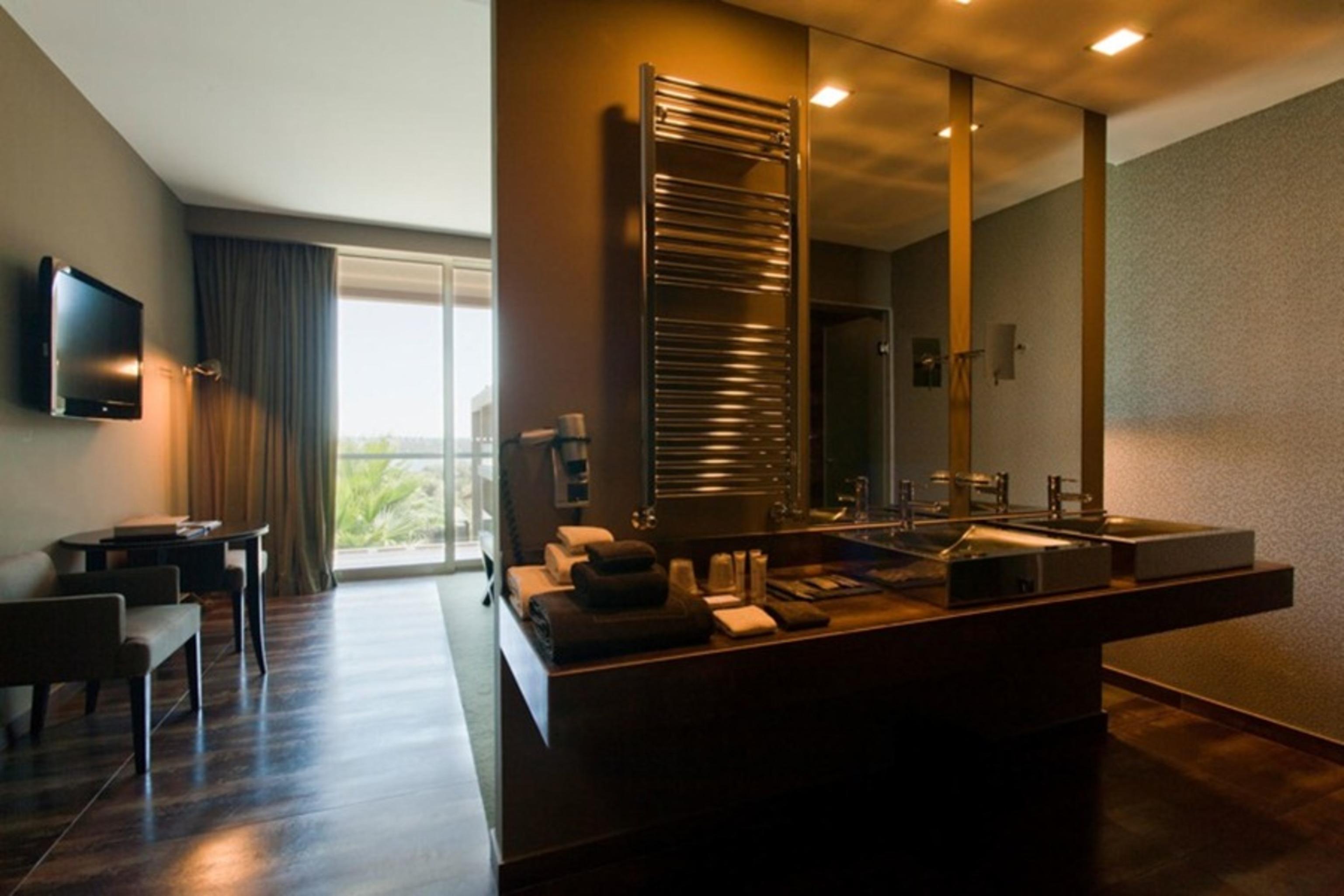 Ap Lago Montargil - Conference & Spa Exterior photo The photo displays a modern hotel room with a contemporary design. The room features a large window, allowing natural light to enter and offering a view outside. On one side, there is a sitting area with a small table and chairs. The other side showc