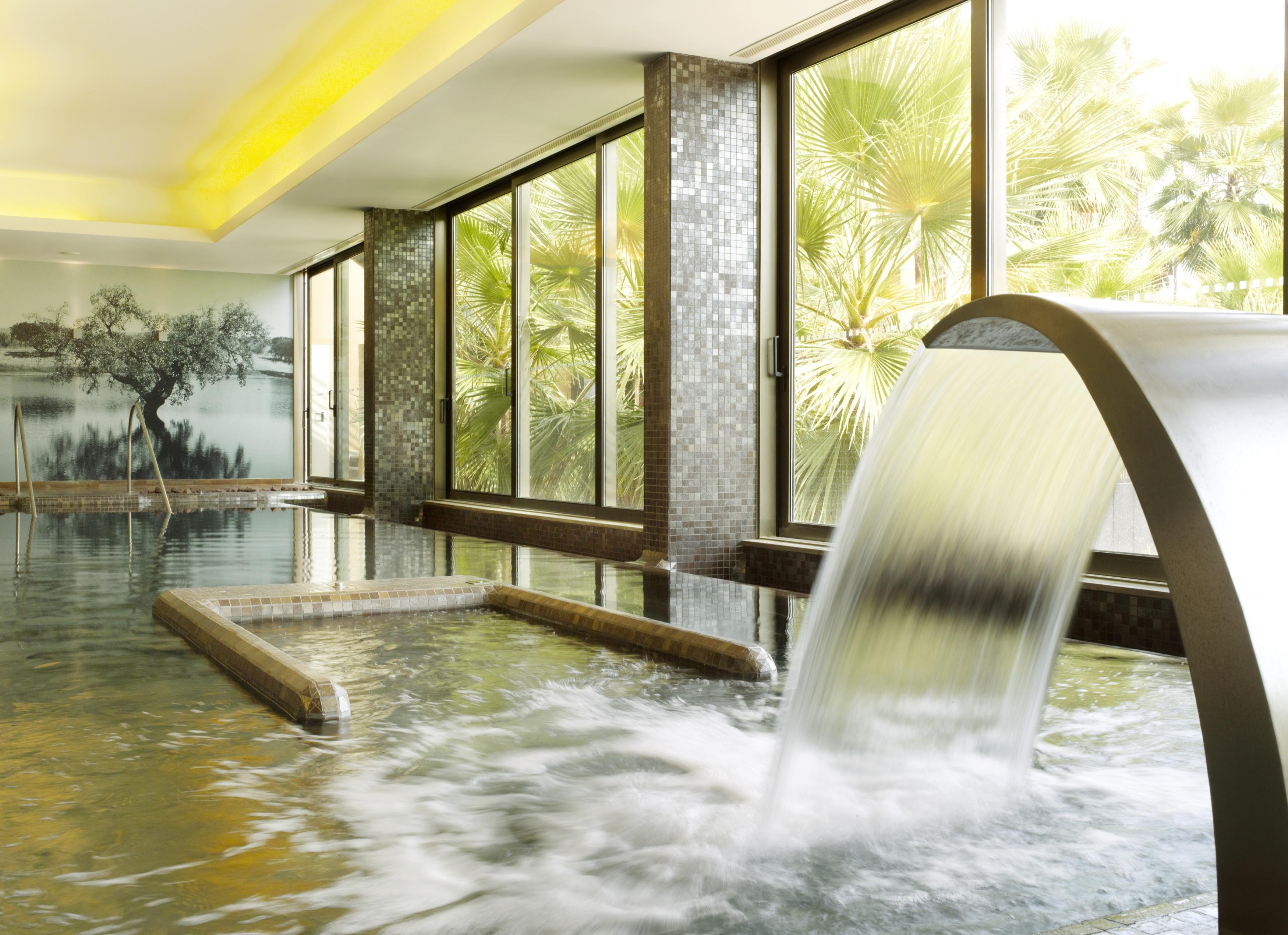 Ap Lago Montargil - Conference & Spa Exterior photo The photo depicts a serene spa environment featuring a tranquil indoor pool area. There is a sleek, modern water feature that spills water gracefully into the pool. Large windows allow natural light to flood the space, showcasing views of lush greene