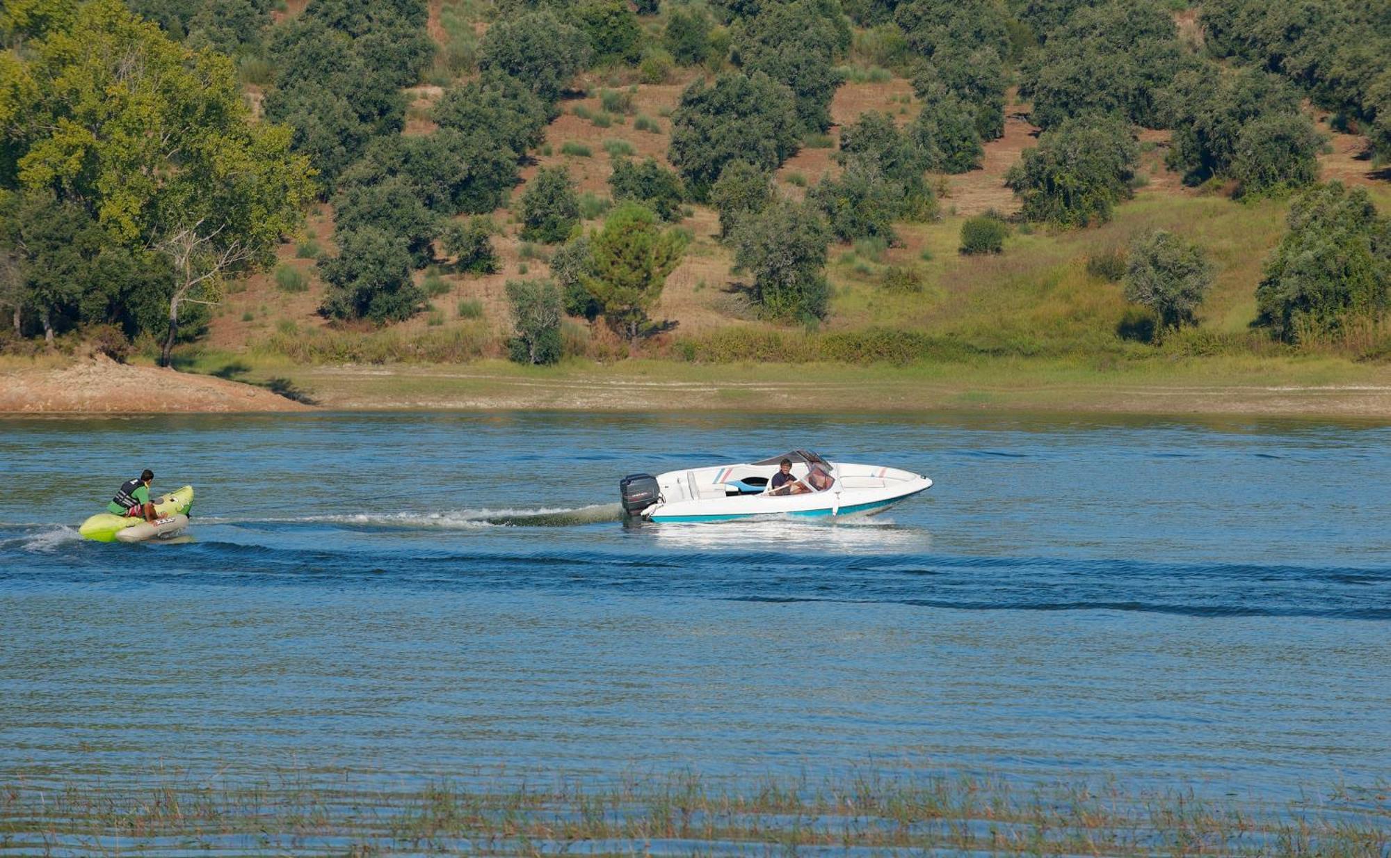 Ap Lago Montargil - Conference & Spa Exterior photo The photo shows a scene on a water body, likely a river or lake. In the foreground, a speedboat is moving quickly through the water, leaving a wake behind it. There are two people visible in the boat. In the background, there is a hilly area covered 